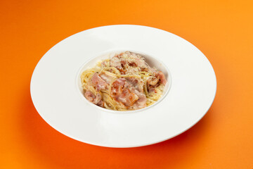 Pasta with bacon in a plate on an orange background.