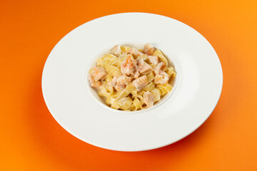 Pasta with salmon in a plate on an orange background.