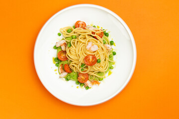 Pasta with shrimp and tomato in a plate on an orange background.
