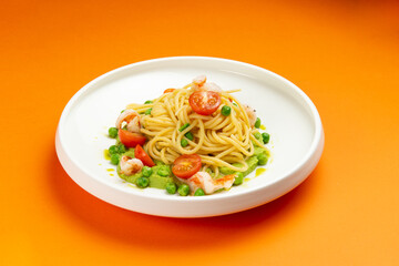 Pasta with shrimp and tomato in a plate on an orange background.