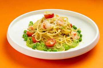 Pasta with shrimp and tomato in a plate on an orange background.