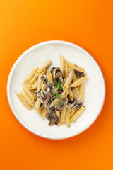 Pasta with mushrooms in a plate on an orange background.