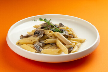 Pasta with mushrooms in a plate on an orange background.