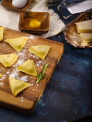 Raw Italian organic ravioli on a cutting board on a dark blue background. The process of making homemade Italian ravioli. Tasty food. healthy lifestyle.