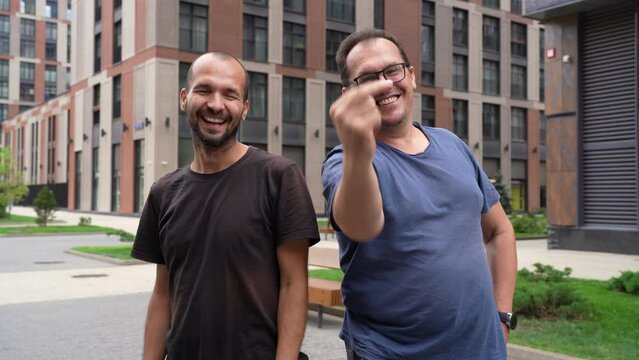 Two funny caucasian men looking at camera and showing fuck off gesture, demonstrating middle finger at street outdoors
