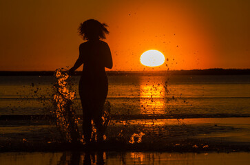 The girl runs on the water at sunset. Bather. Rest on the sea