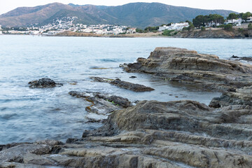 Llança visto desde una playa con rocas en primer plano