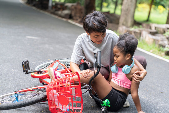 half-African-American girl learning to ride a bicycle has a bicycle accident while learning that an Asian mother comes to help her daughter in the park while she is exercising.