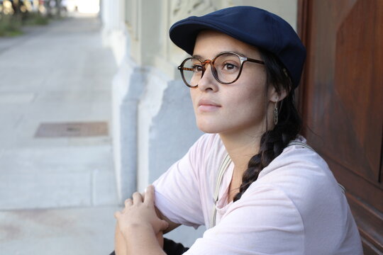 Cute woman wearing vintage style hat and eyeglasses deep in thoughts 