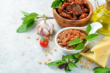 Preparation of traditional Italian pesto sauce with dried tomatoes. Ingredients: basil, parmesan, pine nuts, tomatoes, spices. On a concrete background.