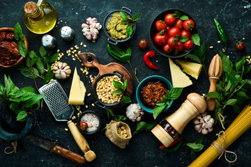 Cooking background: pasta, basil, parmesan, pesto, tomatoes and nuts, olive oil. On a black stone background background.