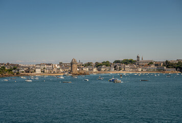Fototapeta na wymiar St. Malo, Brittany, France - July 8, 2022: Cityscape of Saint-Servan neighborhood at its beach on Rance river mouth with left the Solidor towers and right Sainte-Croix church under blue sky. Yachts.