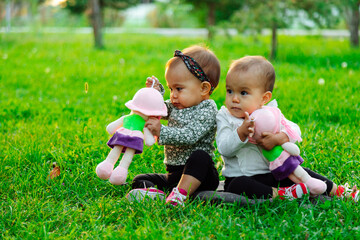 Twin babies playing with doll and sitting on the lawn outside