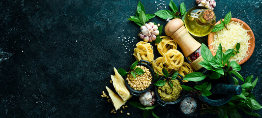 Preparation of pasta with pesto sauce and sun-dried tomatoes. Italian traditional cuisine. On a black stone background background.