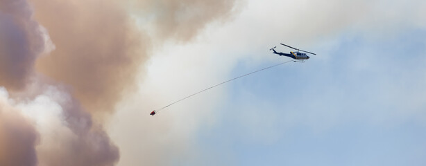 Wildfire Service Helicopter flying over BC Forest Fire and Smoke on the mountain near Hope during a hot sunny summer day. British Columbia, Canada. Natural Disaster