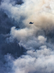 Wildfire Service Helicopter flying over BC Forest Fire and Smoke on the mountain near Hope during a hot sunny summer day. British Columbia, Canada. Natural Disaster