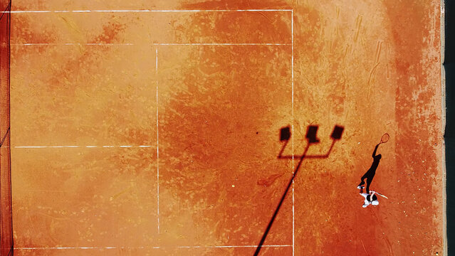 Tennis court drone aerial shot vertical top view, overhead shot of a player shadow silhouette  tennis player on a juicy red coating
