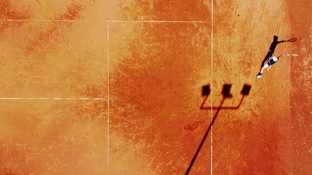 Tennis court drone aerial shot vertical top view, overhead shot of a player shadow silhouette  tennis player on a juicy red coating
