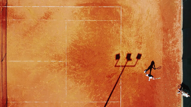 Tennis court drone aerial shot vertical top view, overhead shot of a player shadow silhouette  tennis player on a juicy red coating