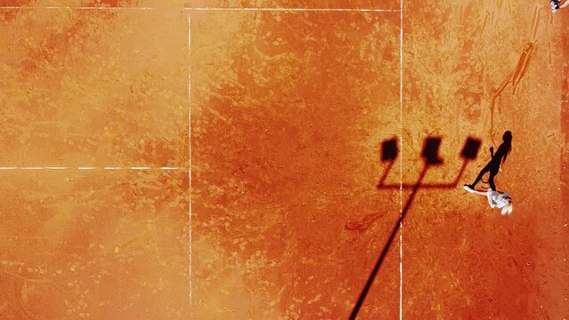 Tennis court drone aerial shot vertical top view, overhead shot of a player shadow silhouette  tennis player on a juicy red coating