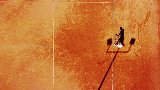 Tennis court drone aerial shot vertical top view, overhead shot of a player shadow silhouette  tennis player on a juicy red coating