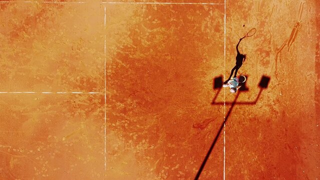 Tennis court drone aerial shot vertical top view, overhead shot of a player shadow silhouette  tennis player on a juicy red coating