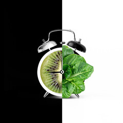 Alarm clock with green leaves of salad and kiwi instead of dial on black and white background. 9 o'clock. Creative trendy collage. Contemporary art. Modern design. Healthy eating, veganism. Inversion 