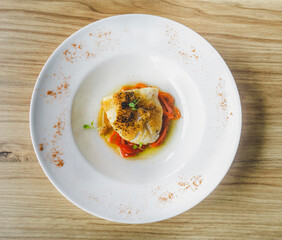 Delicious baked cod with roasted red pepper on wooden table.