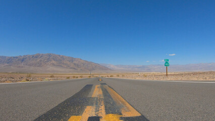 State Route 190 near the Devil's Cornfield area in Death Valley National Park, California, United States. Empty desert road in Death Valley with clear blue sky and rocky mountains.