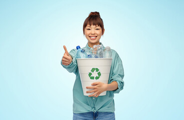 recycling, waste sorting and sustainability concept - smiling young asian woman holding rubbish bin with plastic bottles showing thumbs up over blue background