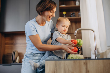 Woman with her son washing vegetables in the kitchen sink