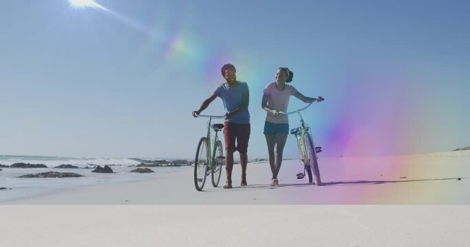Animation of light spots over african american couple with bicycles at beach