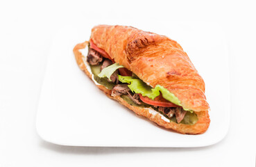 Croissant with beef, pickled cucumber, tomato and lettuce on a white background.
