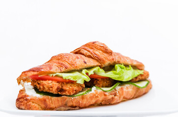 Croissant with chicken cutlet, fresh cucumber, tomato and lettuce on a white background.