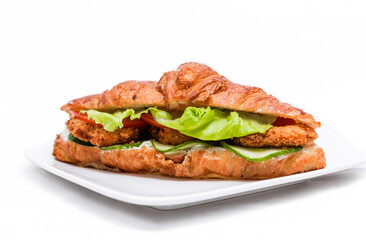 Croissant with chicken cutlet, fresh cucumber, tomato and lettuce on a white background.