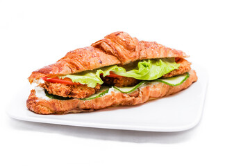 Croissant with chicken cutlet, fresh cucumber, tomato and lettuce on a white background.