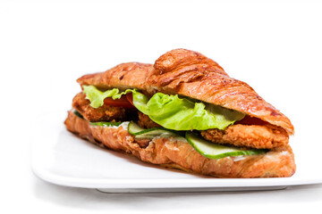 Croissant with chicken cutlet, fresh cucumber, tomato and lettuce on a white background.