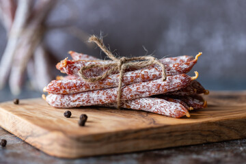 Italian sausage snack. Delicious dry sausage with a bow on a wooden board, black concrete...