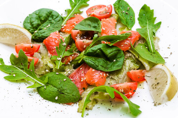 Salad with lightly salted trout, autocados, tomatoes, arugula, spinach and pesto sauce on a white plate.