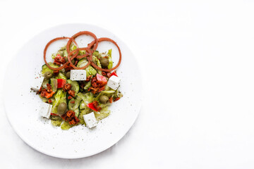 Salad with feta cheese, sun-dried tomatoes, pickled onions with balsamic sauce on a white plate.