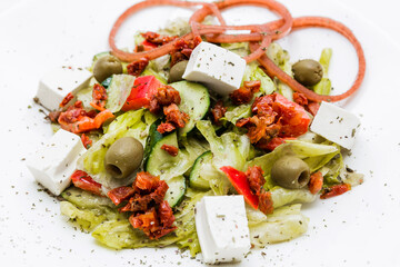 Salad with feta cheese, sun-dried tomatoes, pickled onions with balsamic sauce on a white plate.