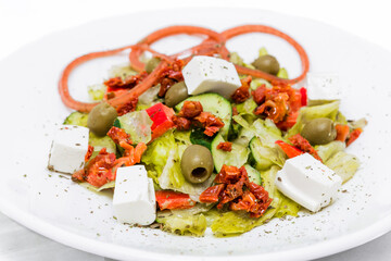 Salad with feta cheese, sun-dried tomatoes, pickled onions with balsamic sauce on a white plate.
