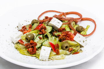 Salad with feta cheese, sun-dried tomatoes, pickled onions with balsamic sauce on a white plate.
