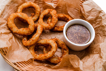 Breaded onion rings with sauce. Served in a wicker basket on craft paper.