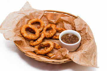 Breaded onion rings with sauce. Served in a wicker basket on craft paper.