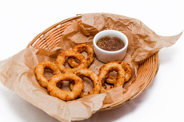 Breaded onion rings with sauce. Served in a wicker basket on craft paper.