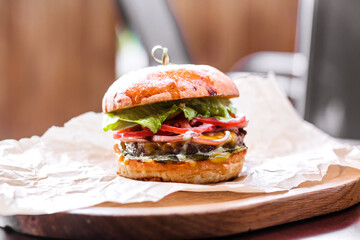 Big tasty beef burger or hamburger on wooden plate with craft paper on wooden table in outdoor...
