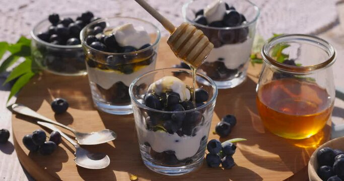 Honey pouring over layered dessert with fresh blueberries and natural yoghurt, close-up view