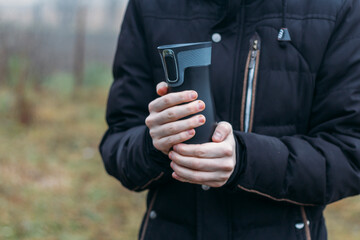 In late autumn, men's hands are warming themselves on a black toggle switch with a hot drink. Environmentally friendly use of reusable glasses, mugs. Rejection of plastic