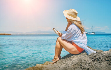 Fashion pretty woman outdoors lifestyle watching, reading on tablet ebook on the beach in summer...